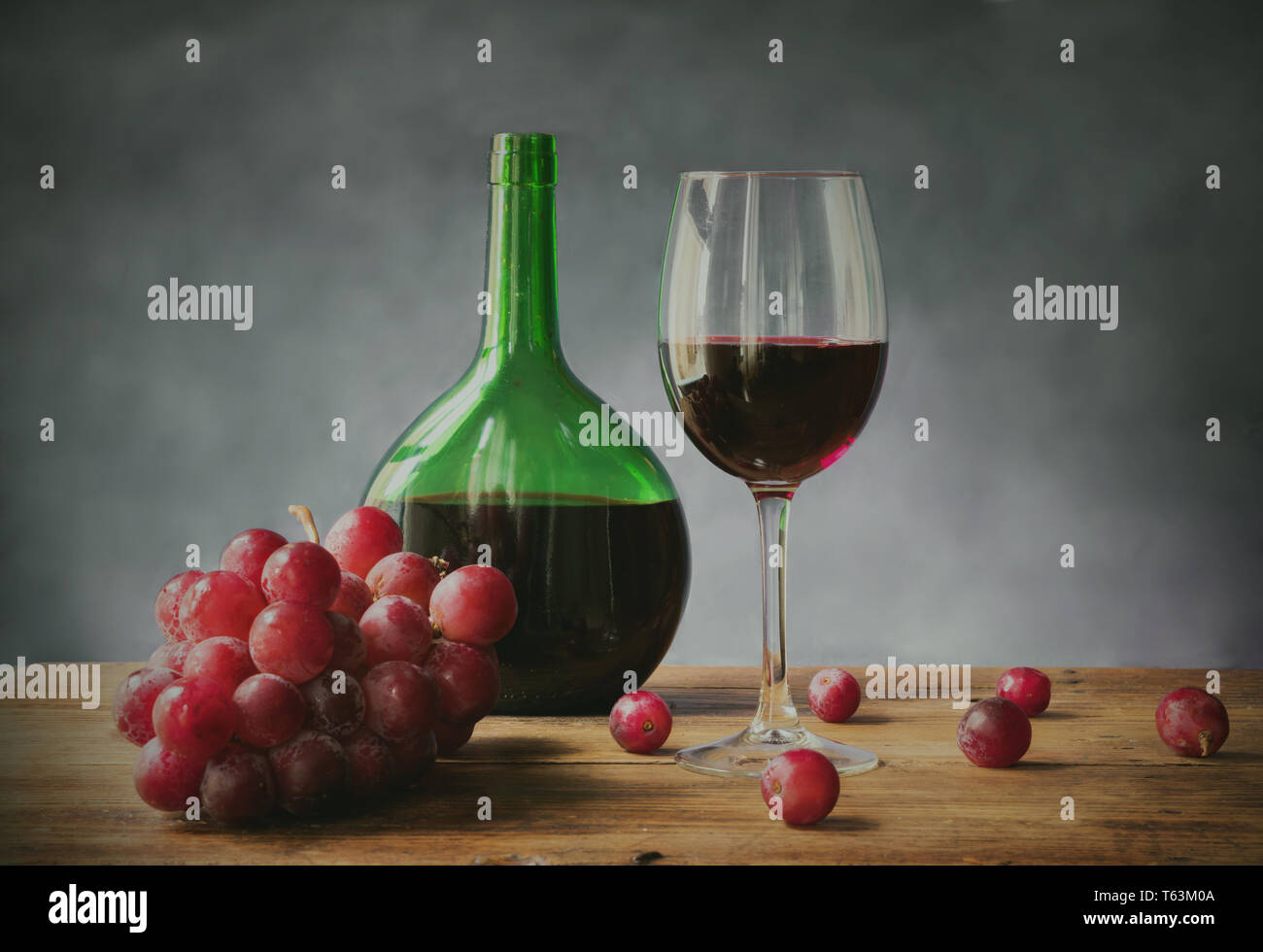 Bicchiere di vino rosso con uve e verde bottiglia di vetro su una vecchia tavola di legno Foto Stock