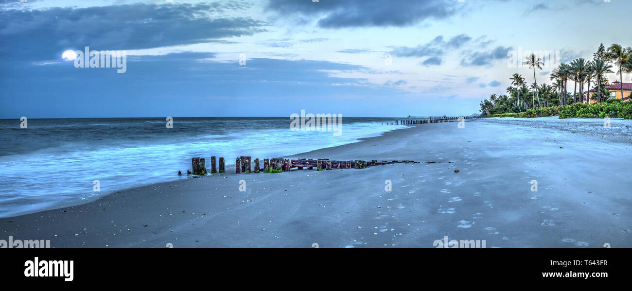 Luna tramonta all'alba su un molo fatiscente sulla spiaggia di Port Royal in Naples, Florida. Foto Stock