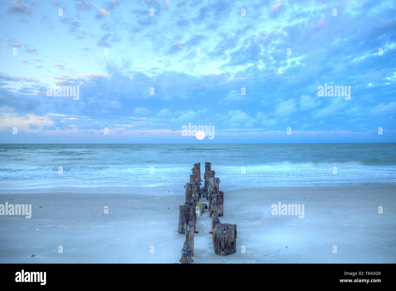 Luna tramonta all'alba su un molo fatiscente sulla spiaggia di Port Royal in Naples, Florida. Foto Stock