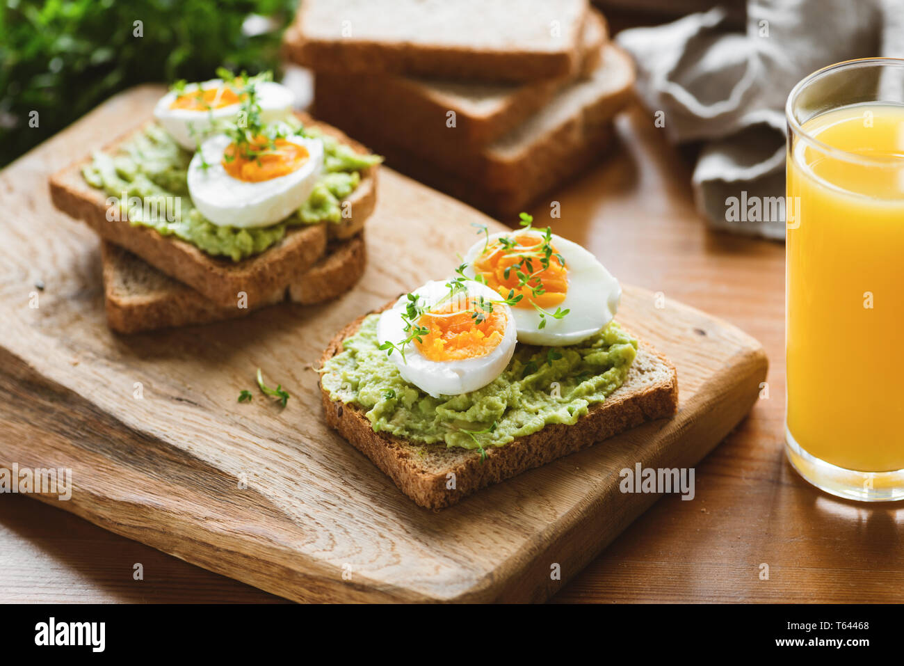 Toast con avocado, uovo, micro verdi e un bicchiere di succo di arancia sul tavolo di legno. Una sana colazione utili Foto Stock