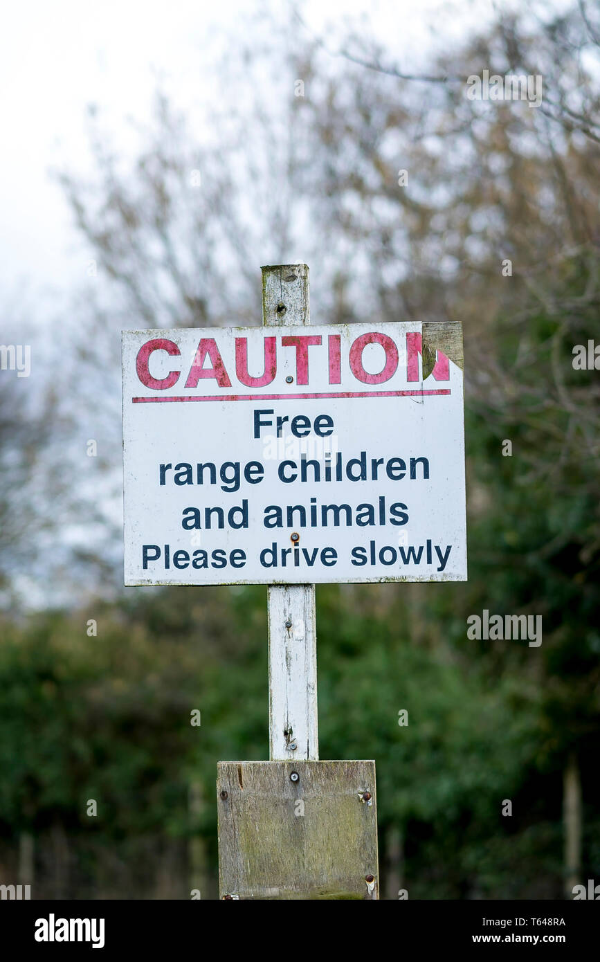 Avviso pubblico avviso per gli automobilisti si prega di guidare lentamente a causa della gamma gratuita I bambini e gli animali nella zona. Buoni consigli britannici con senso dell'umorismo! Foto Stock