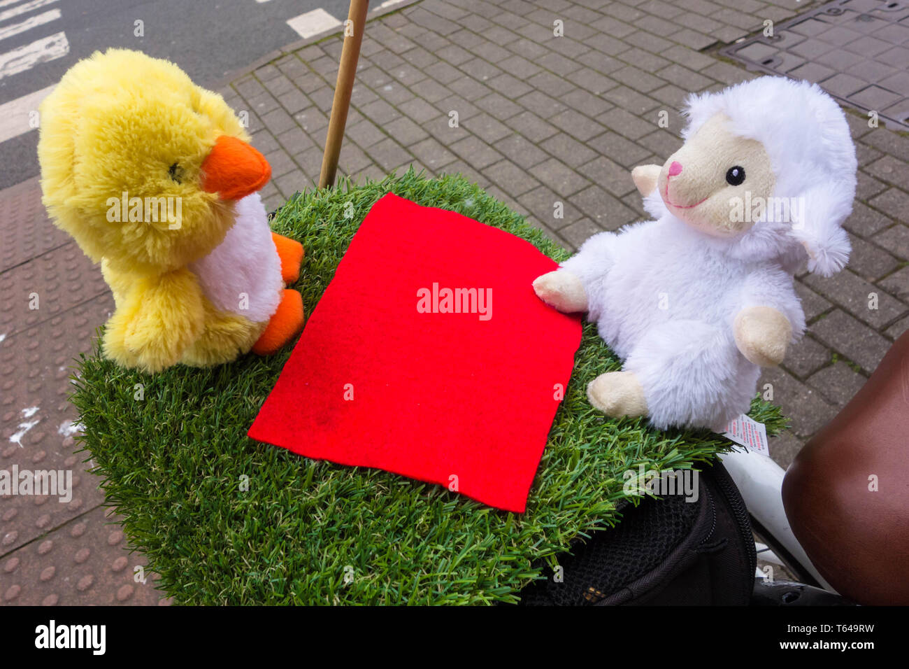 Pulcino e di agnello peluche di sat sul patch di erba in corrispondenza della parte posteriore della bicicletta Foto Stock