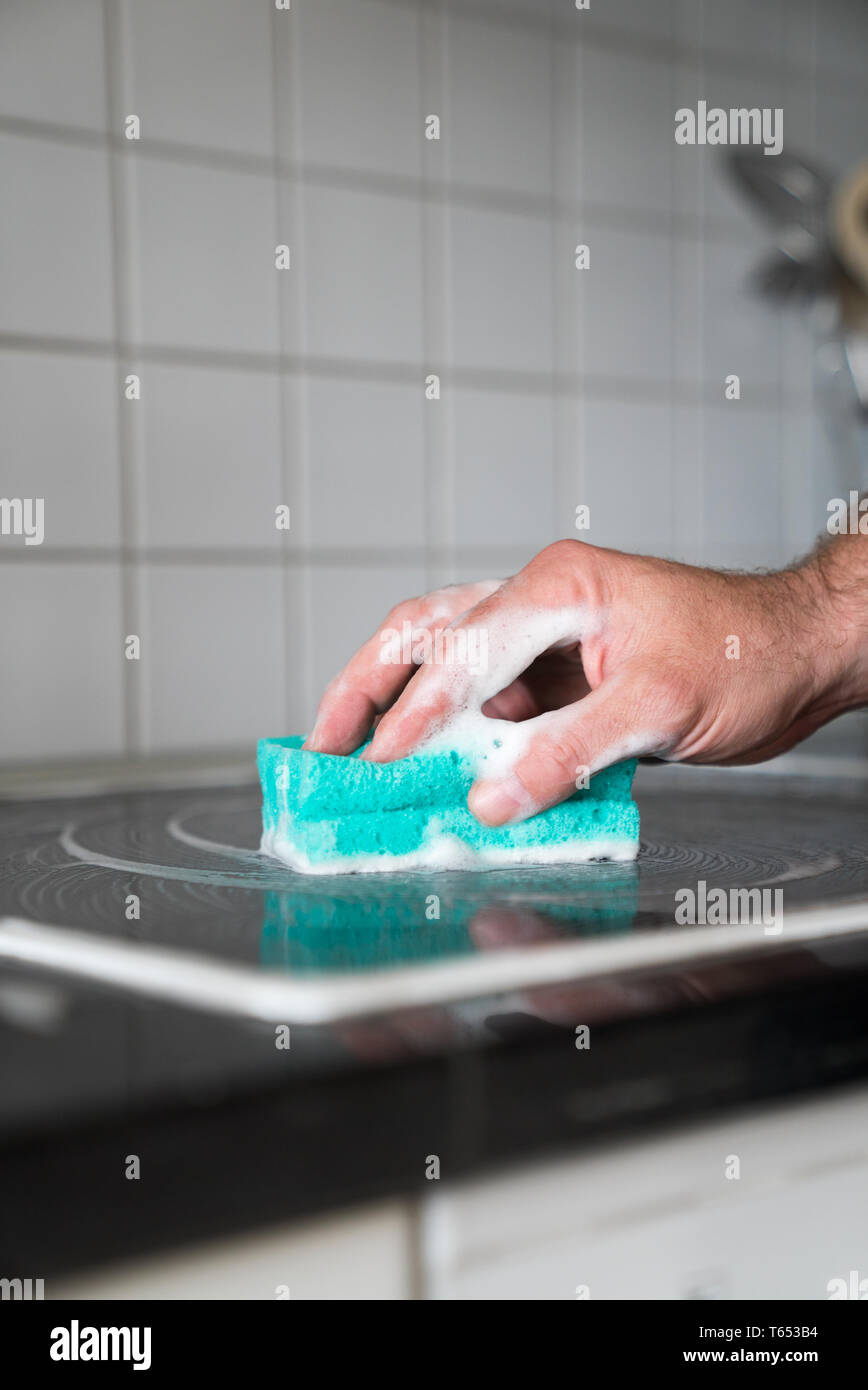 Vista ravvicinata di una moderna casa marito la pulizia di una stufa in cucina con una spugna e un detergente schiumoso Foto Stock