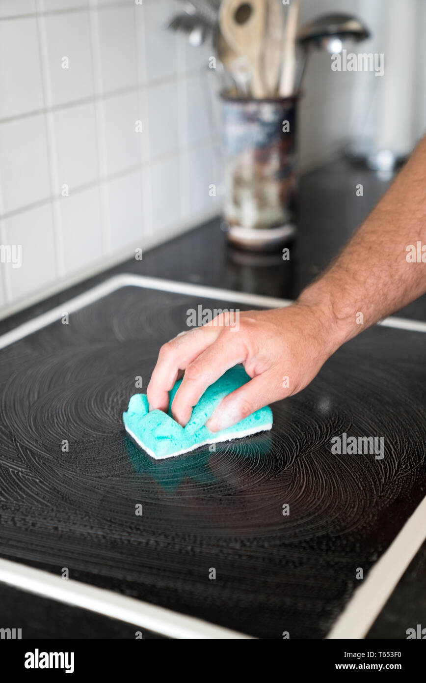 Vista ravvicinata di una moderna casa marito la pulizia di una stufa in cucina con una spugna e un detergente schiumoso Foto Stock