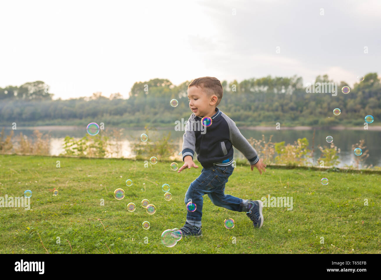 Infanzia, felicità, persone concetto - giovane ragazzo che corre attraverso le bolle di sapone Foto Stock