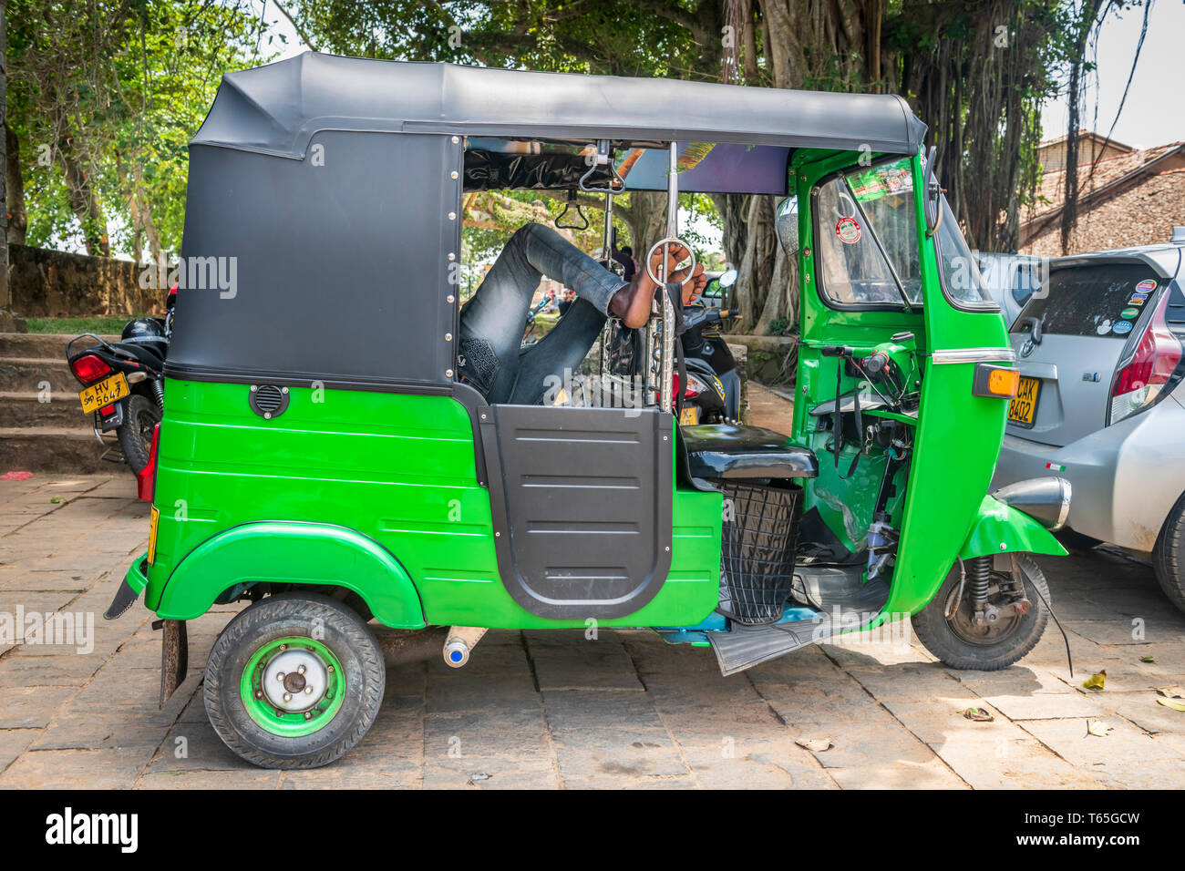 Il conducente di un colore verde brillante Tuk Tuk mette i suoi piedi e si prende una pausa in Sri Lanka città di Galle. Foto Stock
