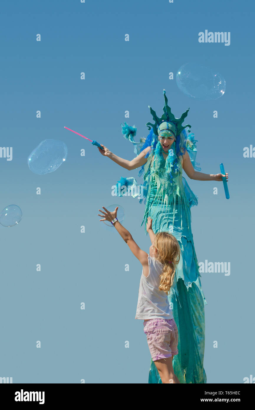 Donna su palafitte con una bolla del ventilatore e una bambina di 7 anni a 8 cercando di catturare le bolle come galleggiano in aria Foto Stock
