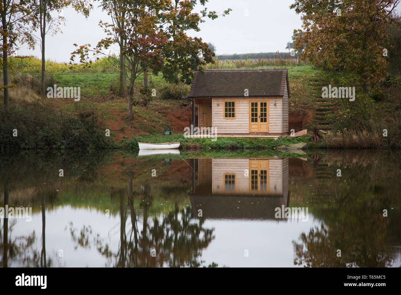 Il lago con la riflessione di alberi e una piccola capanna nautica riflette nel lago che è perfettamente calmo senza un singolo ripple disturbare l'acqua Foto Stock