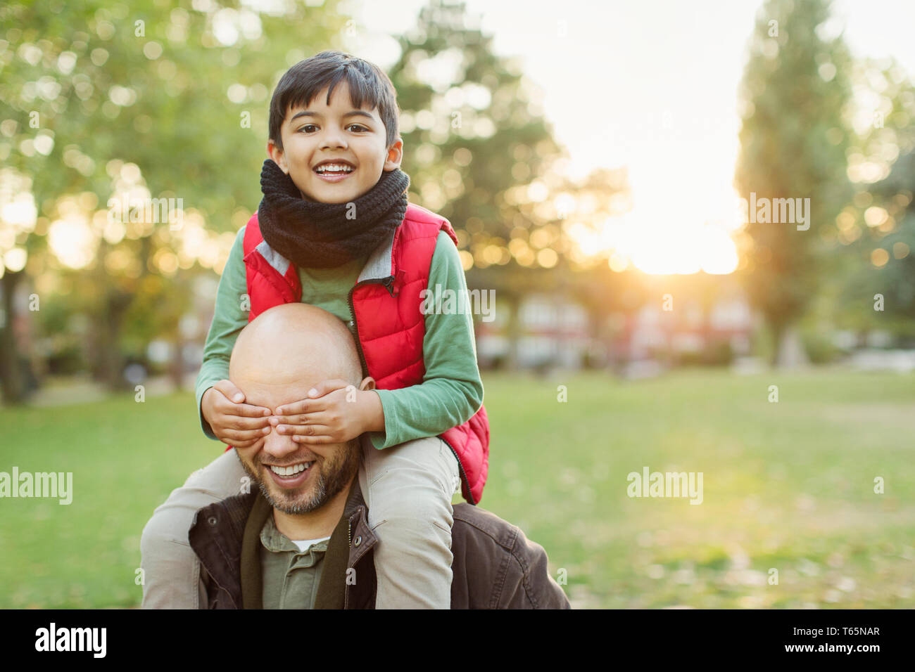 Ritratto giocoso figlio a cavallo sulle spalle dei padri in autunno park Foto Stock