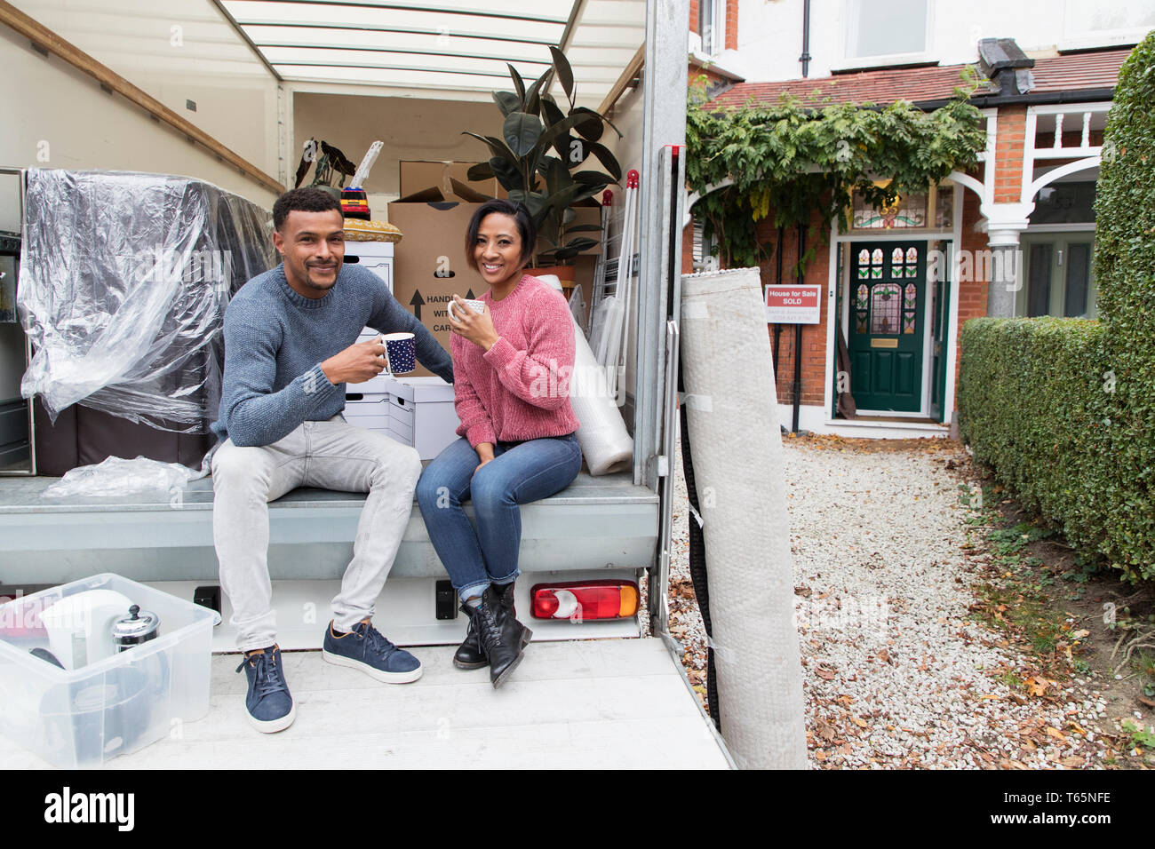 Ritratto felice coppia bere il tè, prendendo una pausa dal muoversi verso la parte posteriore del furgone in movimento Foto Stock