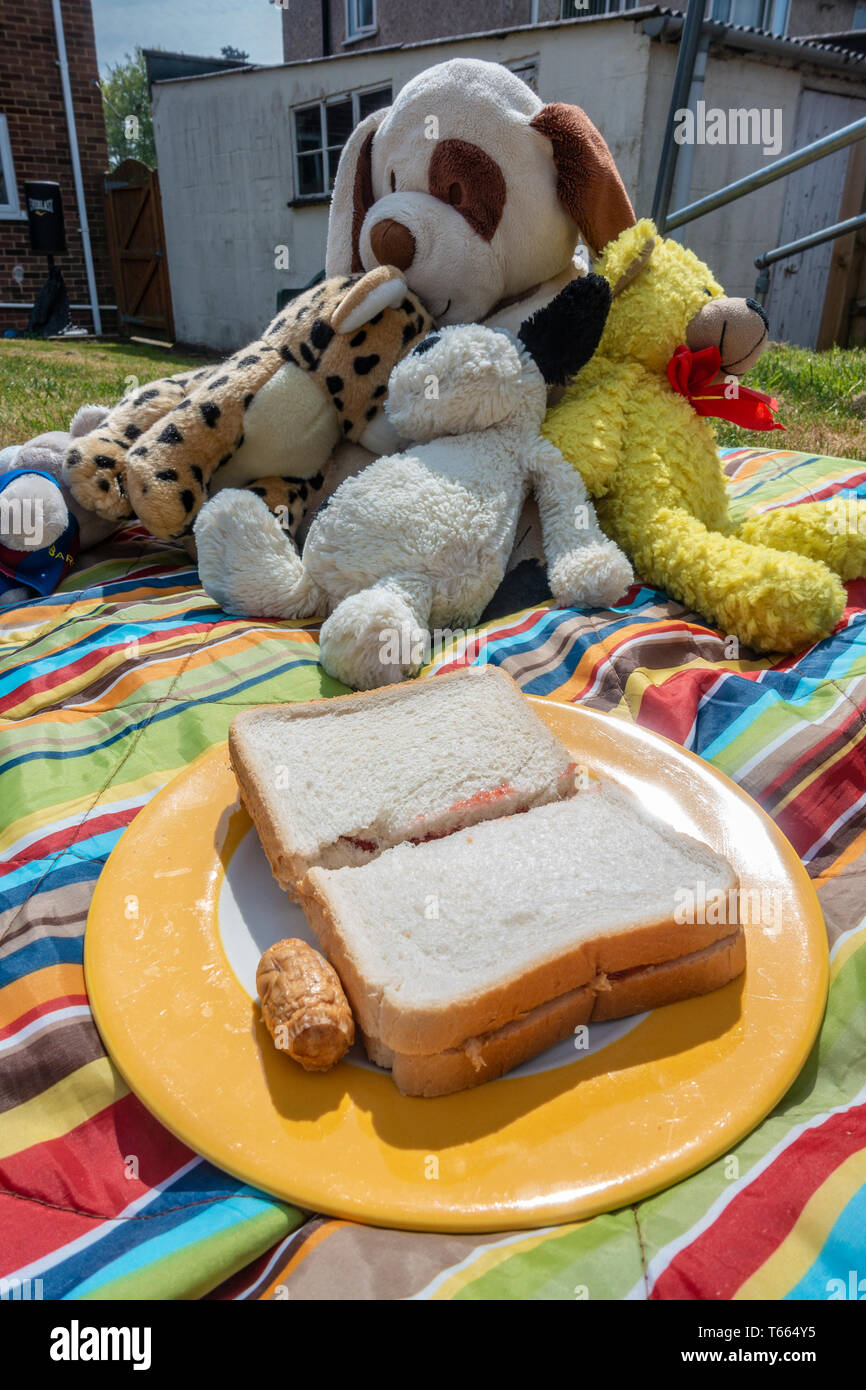 Una piastra con un sandwich di marmellata e un cocktail insaccato su una coperta picnic al di fuori di un orso di peluche di picnic in un giardino sul retro in tempo soleggiato Foto Stock