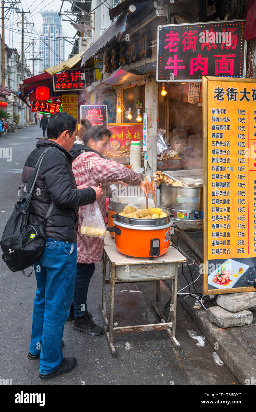 Shanghai, cibo di strada. Giovane acquisto di cibo in un cibo tradizionale stallo nella Città Vecchia, Shanghai, Cina Foto Stock