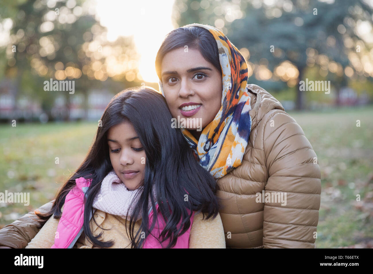 Ritratto sorridente madre in hijab seduto nell'autunno del parco con la figlia Foto Stock