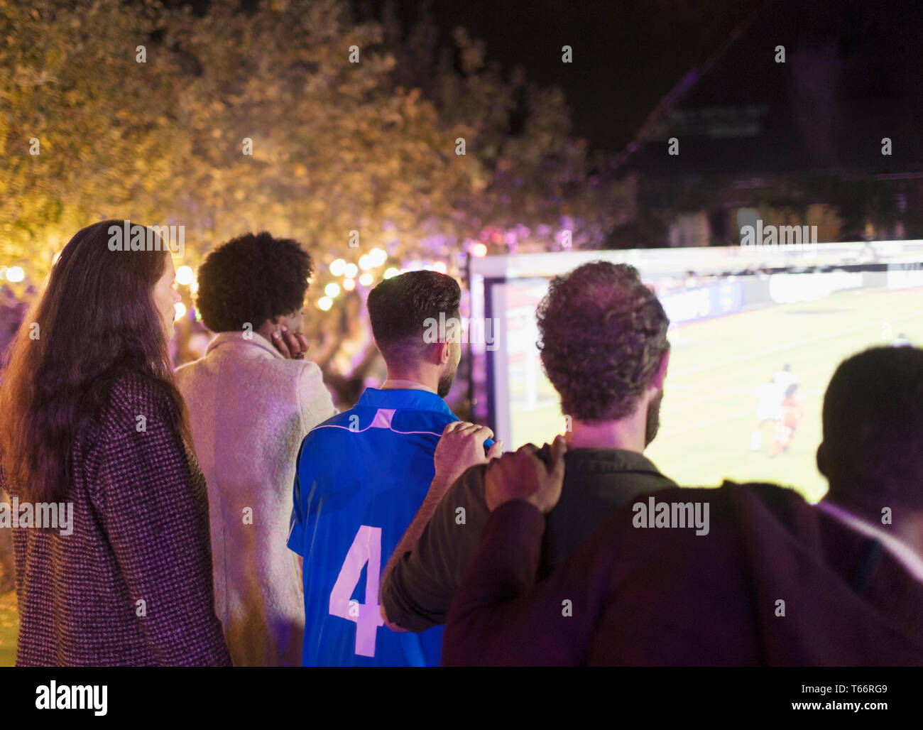 Gli amici a guardare le partite di calcio su schermo di proiezione nel cortile posteriore Foto Stock