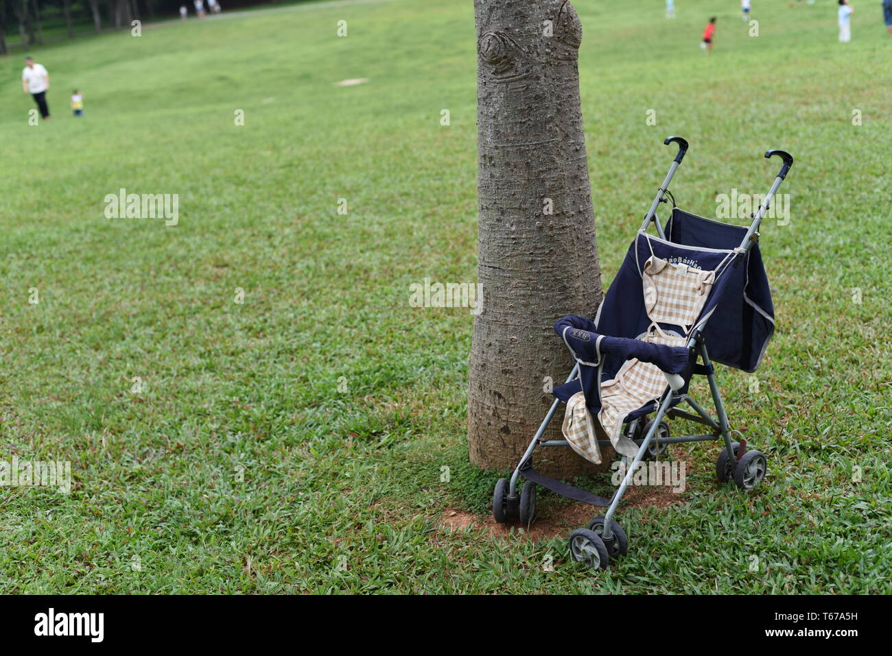 In questa foto si è focalizzato su un servizio baby carrello posto vicino ad un albero in erba, con alcuni adulti che giocano nel parco con i loro figli. Foto Stock