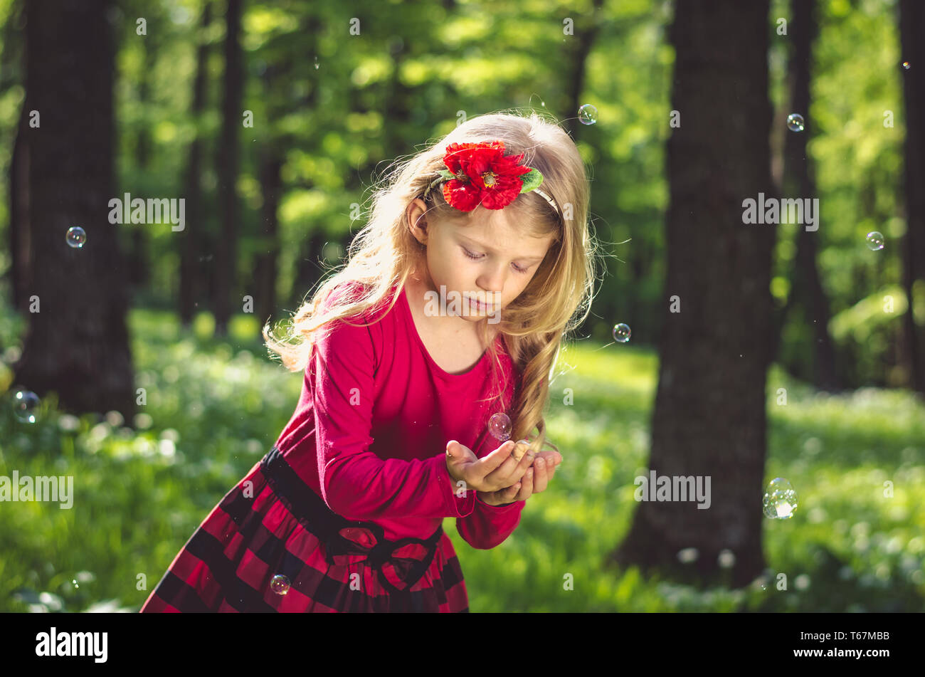 Bella ragazza bionda a giocare con le bolle di sapone all'aperto nel verde della foresta di primavera Foto Stock