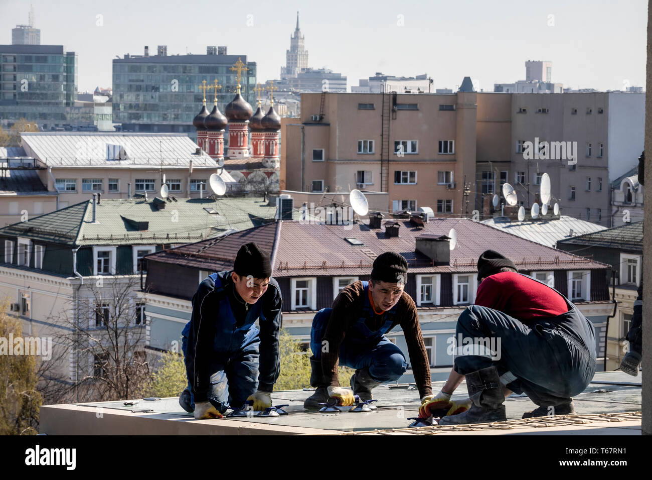 I lavoratori provenienti dalle repubbliche dell' Asia centrale riparare il tetto di un edificio per uffici nel centro di Mosca, Russia Foto Stock