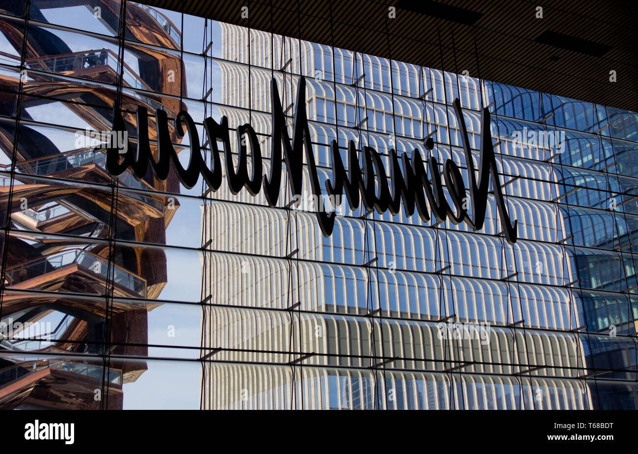 Sulla sinistra il temporaneo nave scultura in acciaio con persone in piedi su di esso, visibile dall'interno della Hudson Yards mall, shot attraverso il retro di un Neiman Marcus segno nella finestra di un edificio in costruzione a destra. L'interactive nuovo segno distintivo composto da interconnessi rampe di scale è stato progettato da architetto britannico Thomas Heatherwick come punto focale dei nuovi cantieri di Hudson complesso, che ha debuttato il 15 marzo 2019, a controversie circa il fatto che esso era troppo elitario. Lo sviluppo comprende retail residenziale, di ristoranti e di istituzioni culturali e spazi pubblici. Foto Stock