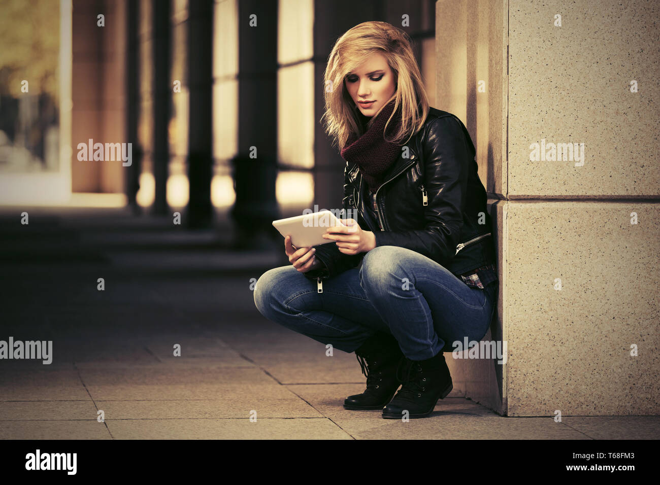 Moda giovane donna con tavoletta digitale sulla strada di città elegante modello femminile vestita di nero giacca di pelle e jeans blu Foto Stock