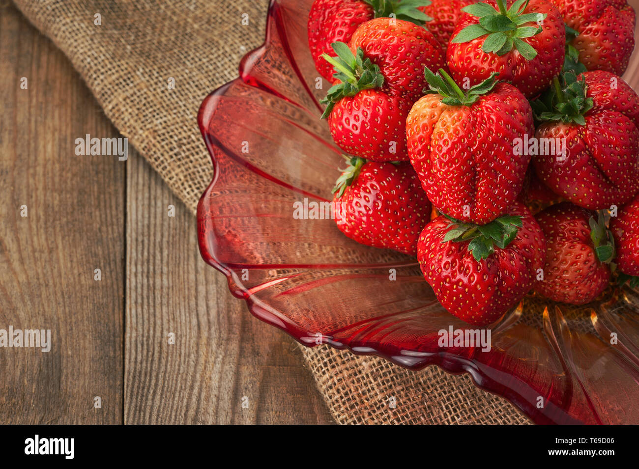 Fresche fragole mature in recipiente di vetro su sfondo di legno. Foto Stock