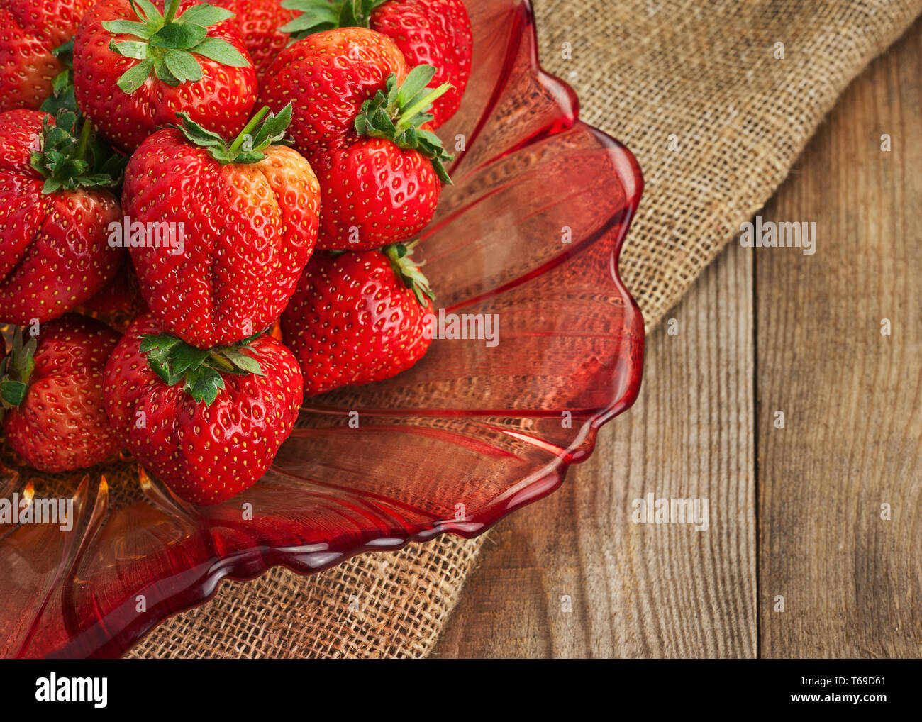 Fresche fragole mature in recipiente di vetro su sfondo di legno. Foto Stock