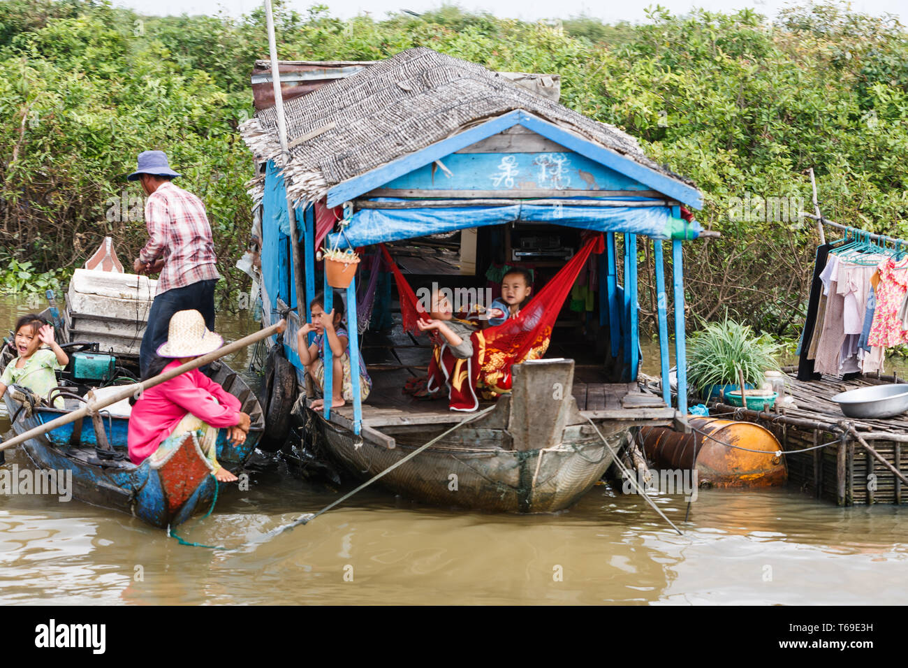 Primo piano della piccola barca casa sul bordo della giungla legato in fiume con quattro figli e genitori in bamboo dock con asciugabiancheria e servizio lavanderia Foto Stock