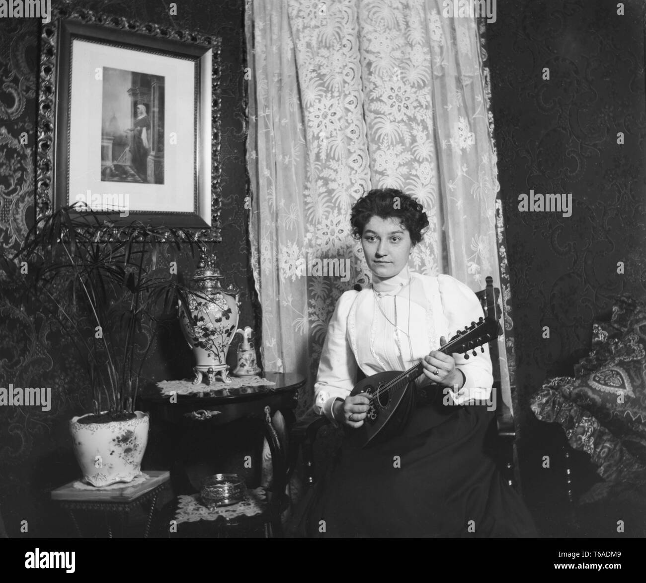Una giovane donna svolge il suo mandolino in salotto, ca. 1910. Foto Stock