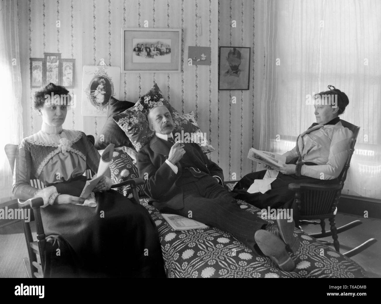 Padre si rilassa con un sigaro mentre la moglie e la figlia godere le loro copie del Connecticut rivista trimestrale, ca. 1900. Foto Stock