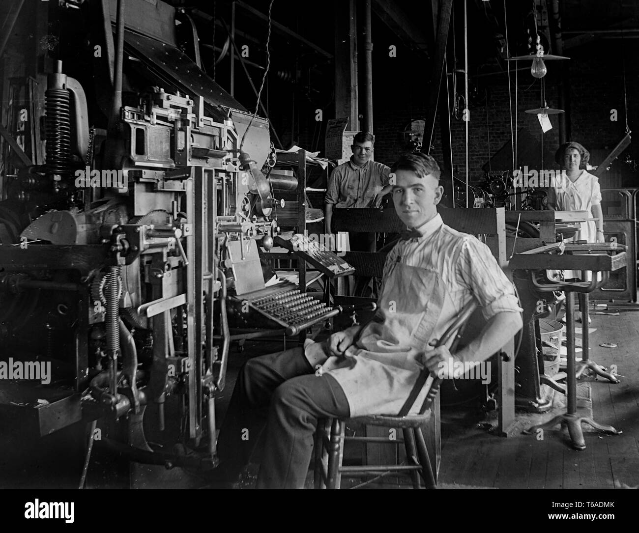 Un giovane uomo si siede in una macchina tipografica nel retro del negozio di un quotidiano della Pennsylvania, ca. 1910. Foto Stock