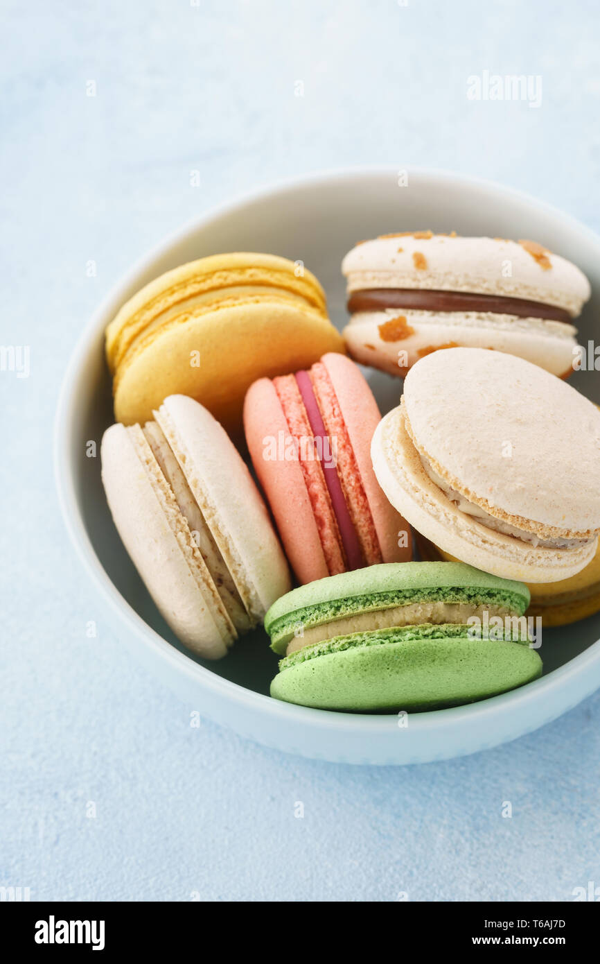 Colorati macarons francese con diversi riempimenti in una ciotola su sfondo blu. Foto Stock