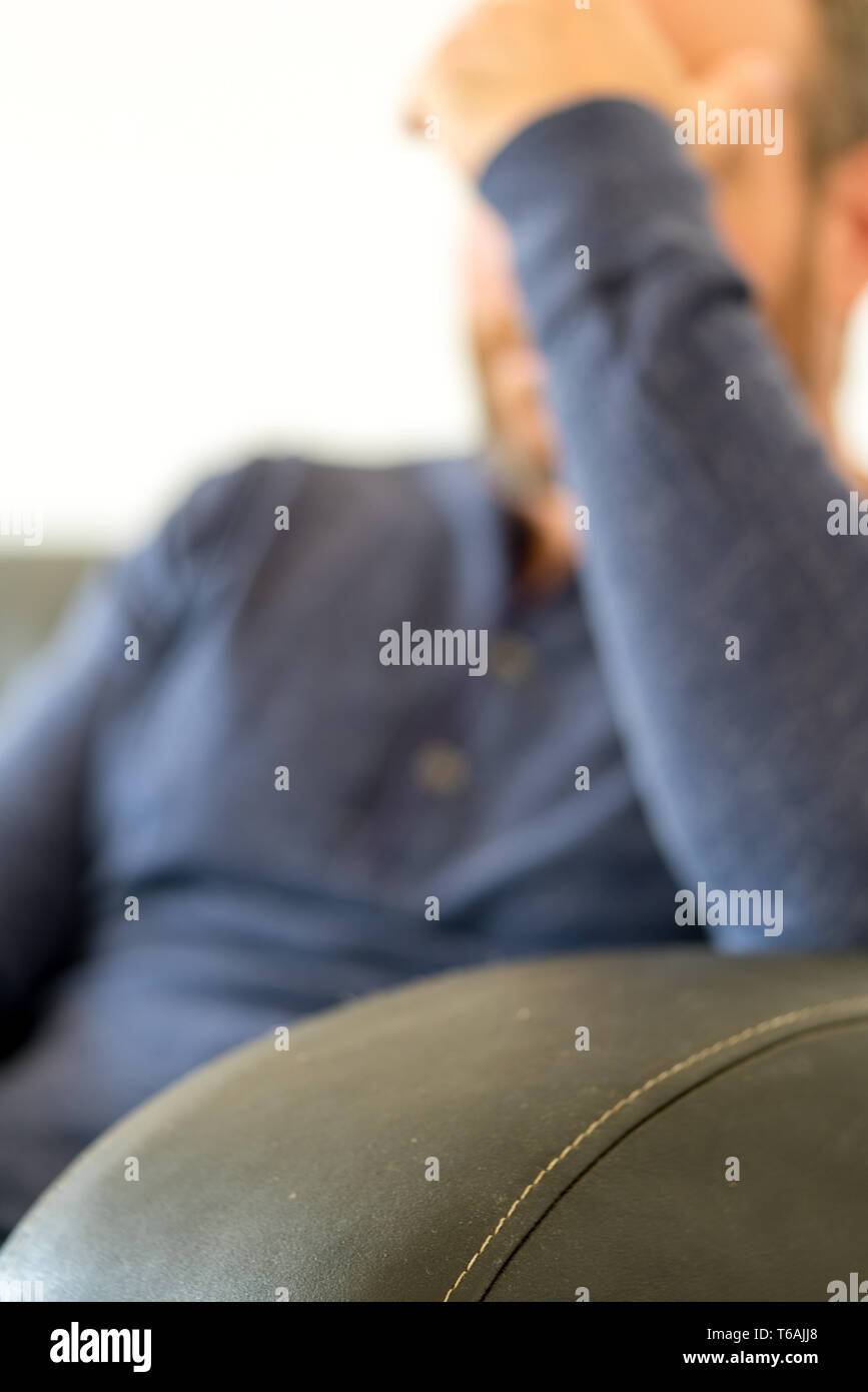Esaurito uomo di mezza età con la barba si siede sul divano e appoggia la sua testa stanca nella sua mano messa a fuoco selettiva Foto Stock
