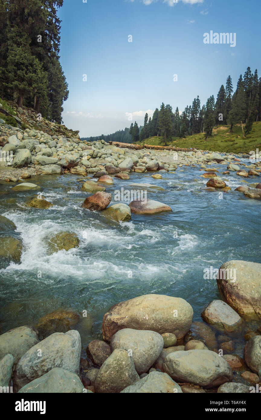 Un cristallo chiaro con flusso di acque blu che scorre attraverso un ampia valle di montagna in Doodhpathri, Kashmir. Grandi massi in un veloce flusso di movimento Foto Stock