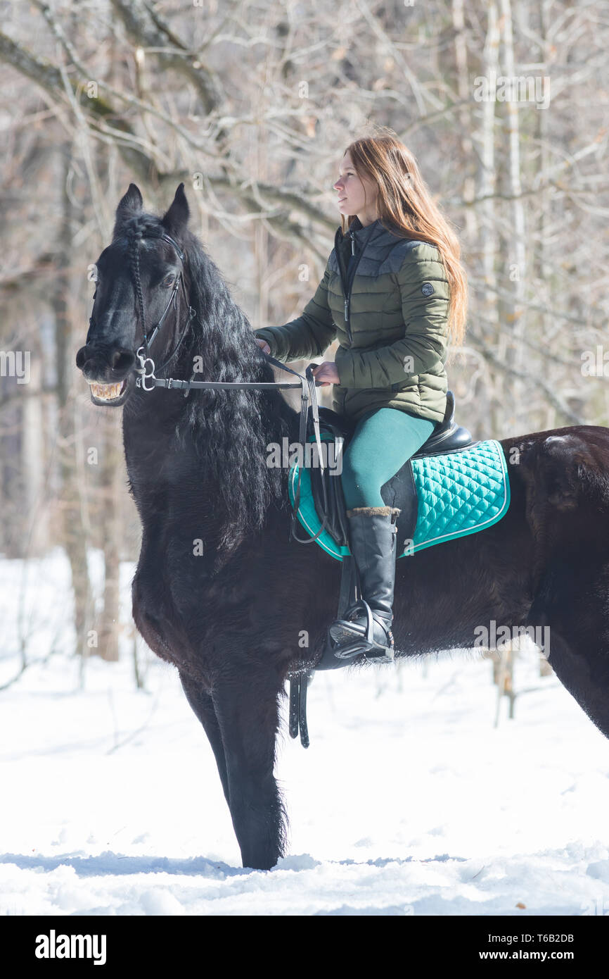 Un bosco d'inverno. Una donna con lunghi di indossare la giacca verde  capelli a cavallo di un colore marrone scuro cavallo Foto stock - Alamy