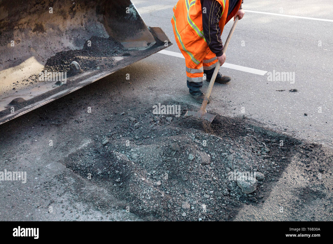 La manutenzione stradale lavoratore getta il vecchio asfalto in dell'escavatore carrello in strada in costruzione Foto Stock