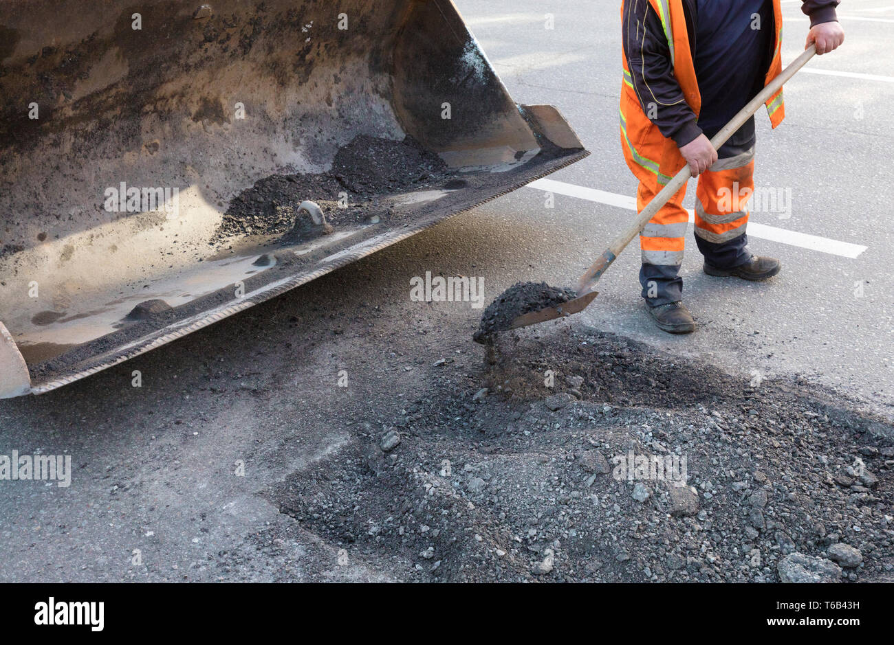 La manutenzione stradale lavoratore getta il vecchio asfalto in dell'escavatore carrello in strada in costruzione Foto Stock