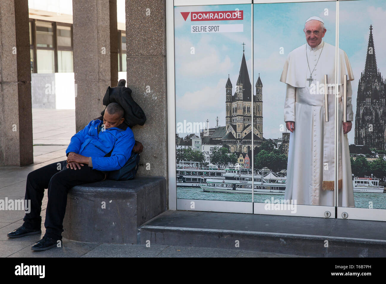 L'uomo avente un pisolino vicino a piazza del duomo, poster con Papa Francesco, Colonia, Germania. Mann haelt ein Nickerchen auf der Domplatte, Plakat mit Pa Foto Stock