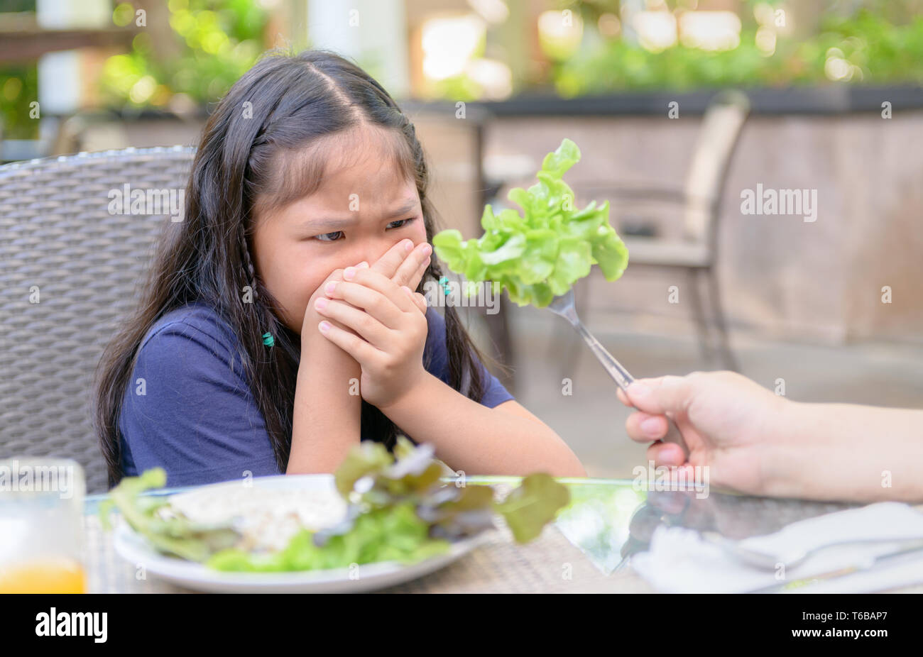 Bambino asiatico ragazza con espressione di disgusto contro le verdure in insalata, rifiutando il concetto di cibo Foto Stock
