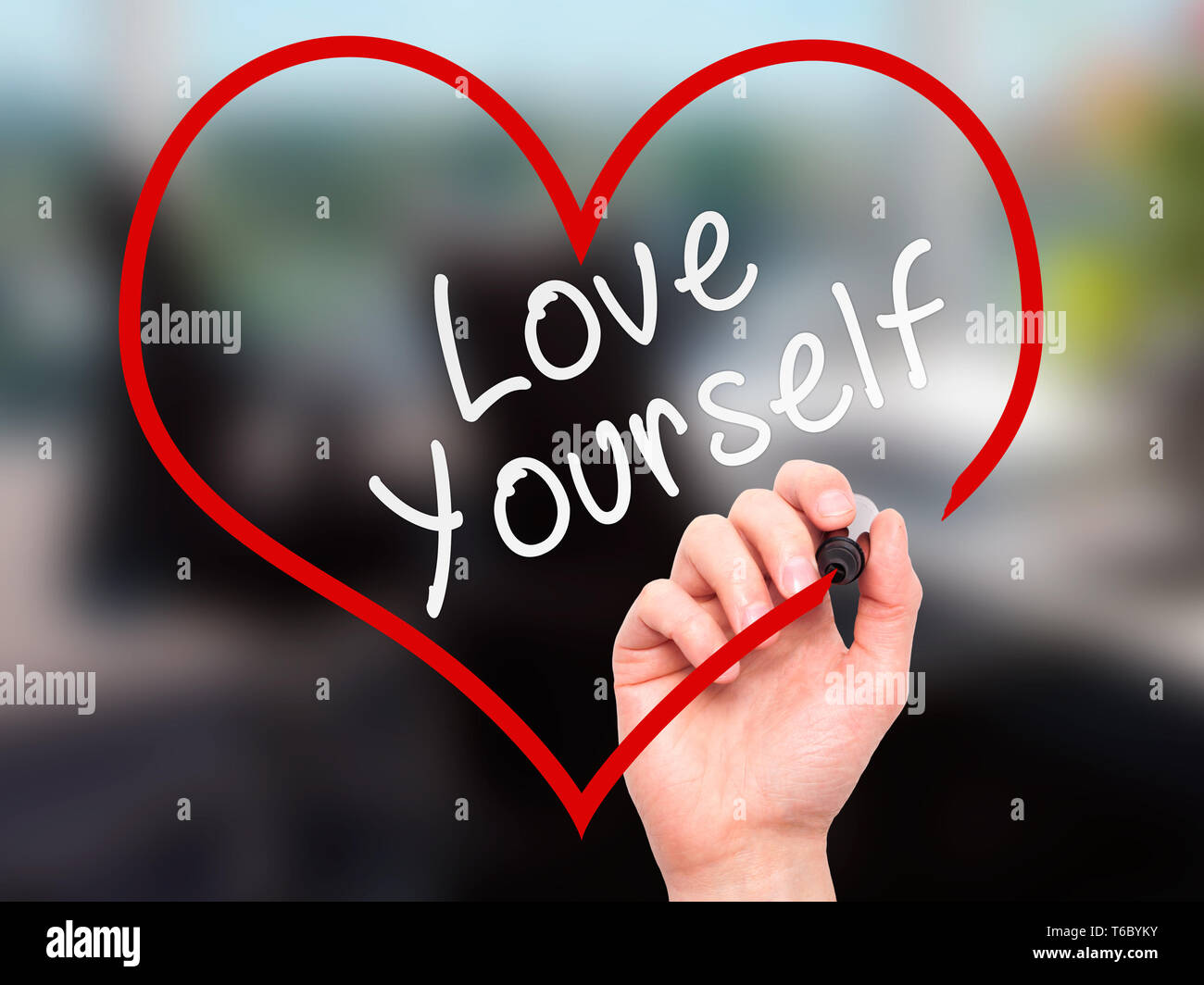 Man mano che scrive amare voi stessi con un pennarello sulla cancellazione trasparente di bordo, all'interno di forma di cuore Foto Stock