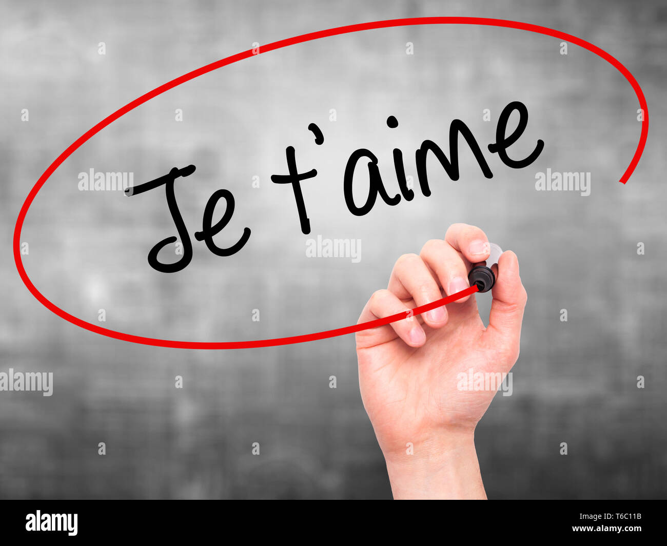 Man mano che scrive Je t'aime ( ti amo in francese) con pennarello nero su schermo visivo Foto Stock