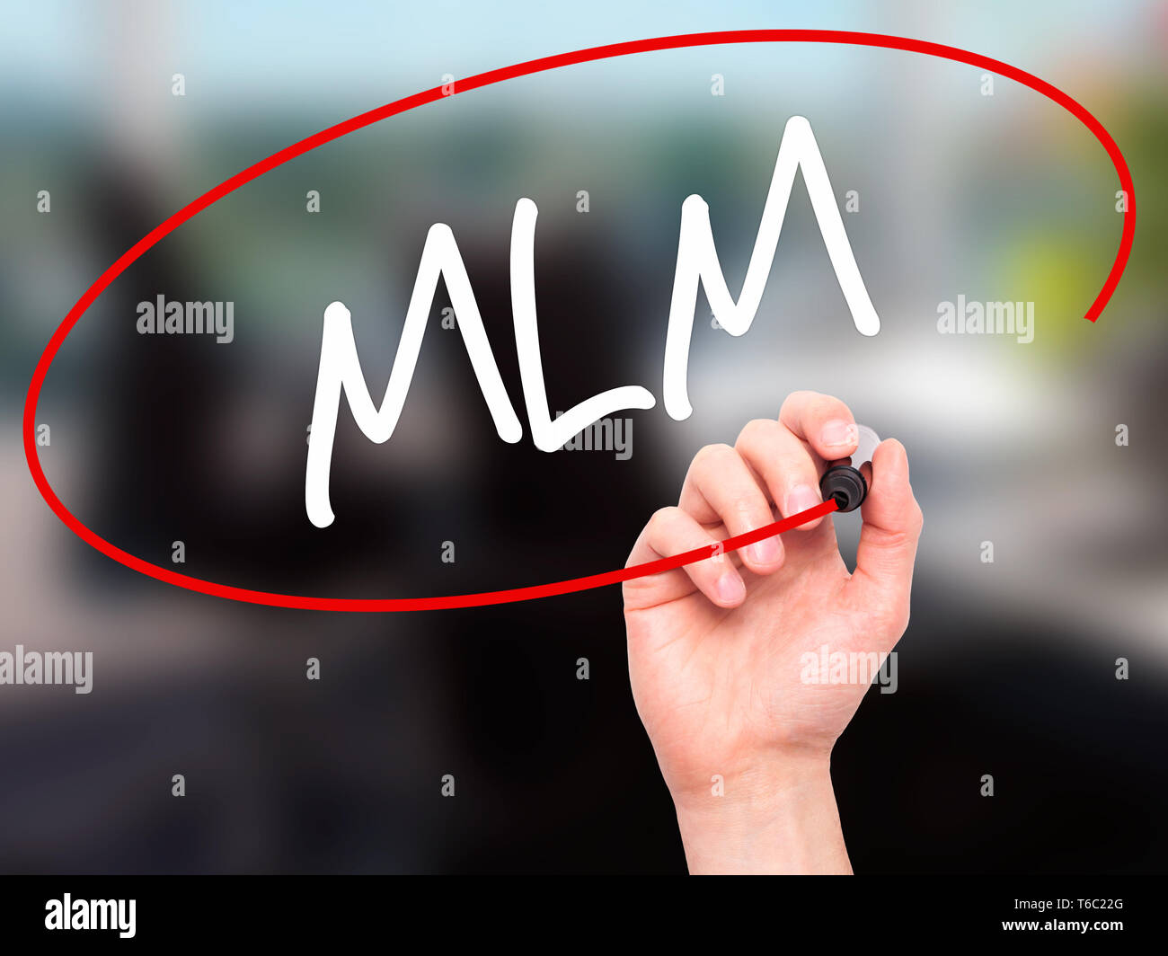 Man mano che scrive MLM (Multi-Level Marketing) con pennarello nero su schermo visivo Foto Stock