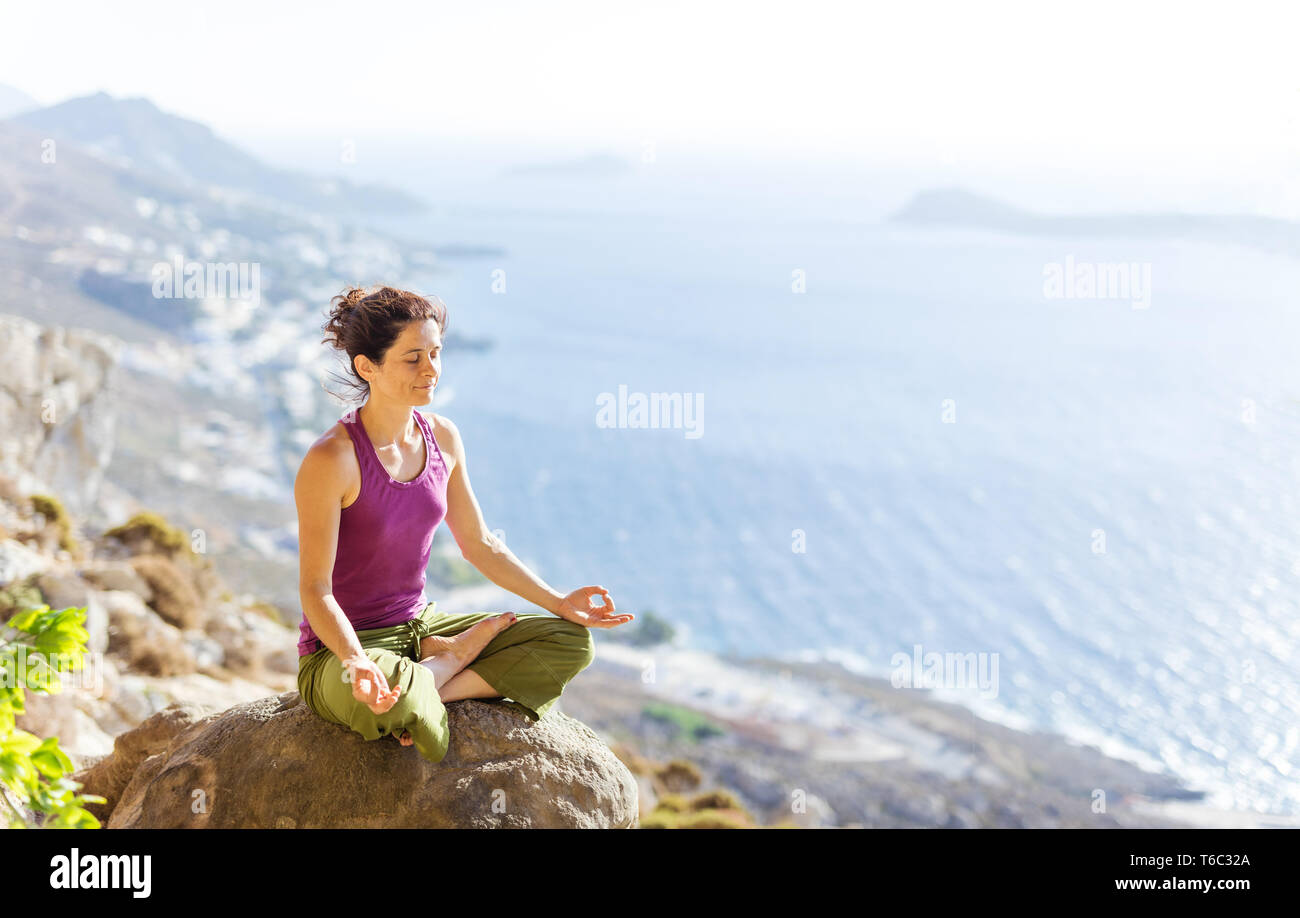 Caucasian giovane donna a praticare yoga mentre è seduto in lotus pongono a picco sul mare Foto Stock