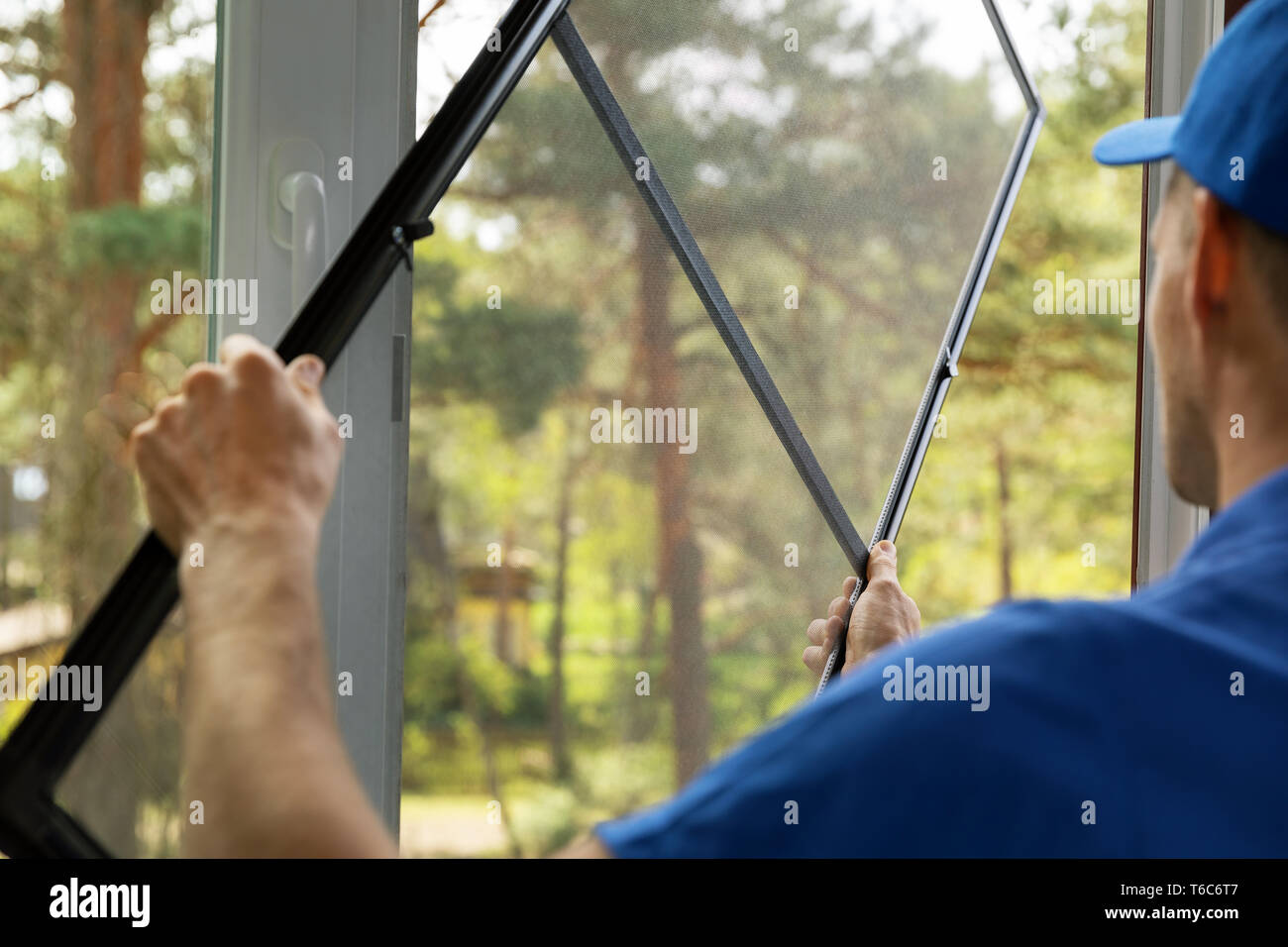 L'uomo installazione zanzariera wire mesh sulla finestra di casa Foto Stock