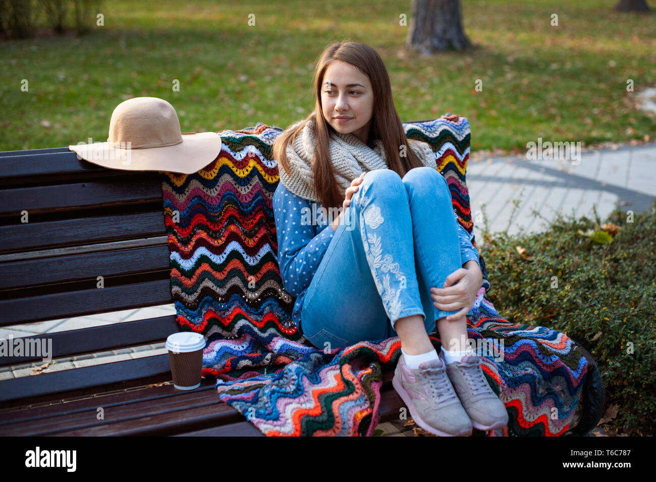 Giovane e attraente ragazza seduta su una panchina nel parco in autunno con il caffè. Foto Stock