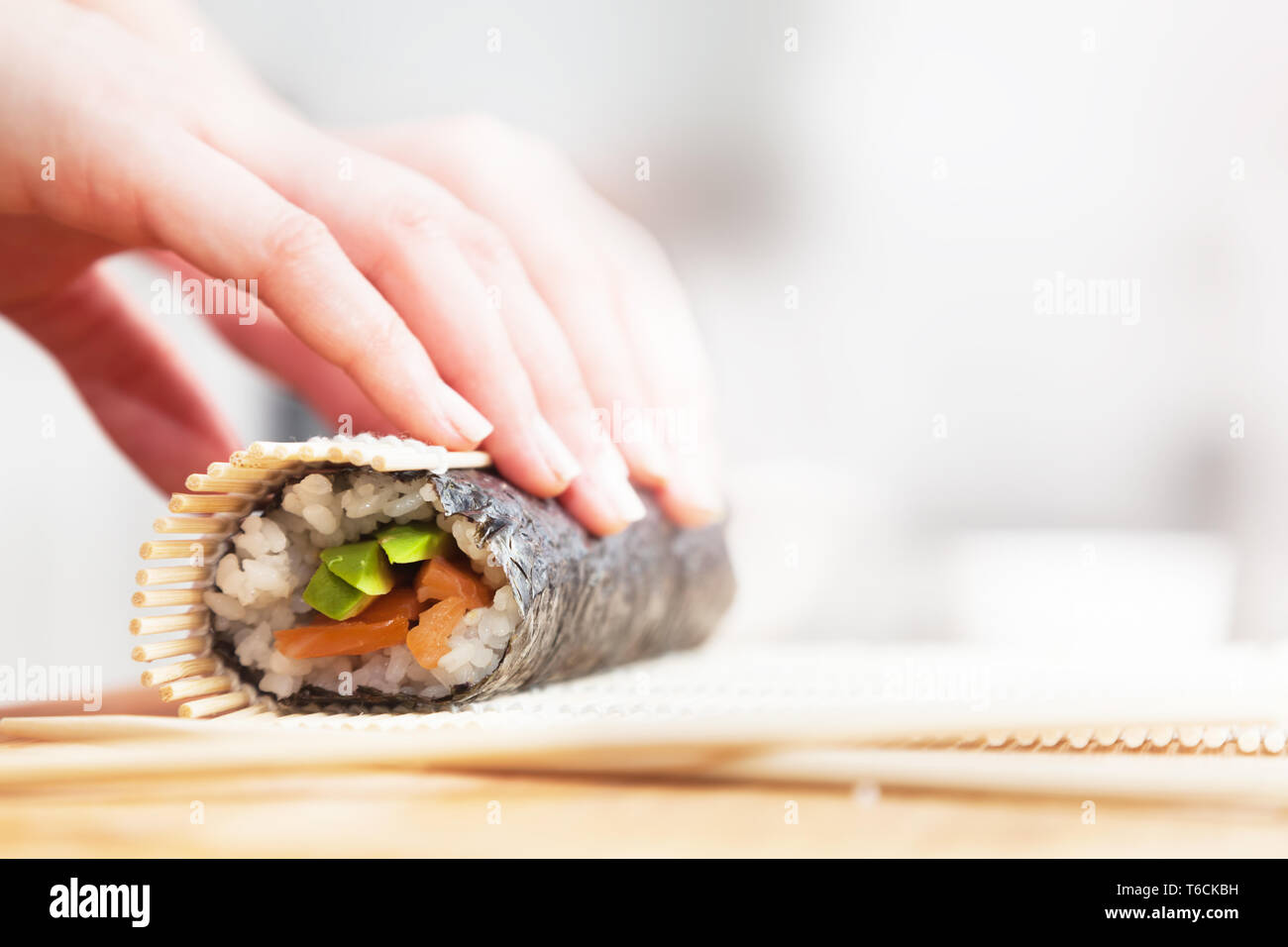 Preparazione, laminazione sushi. Salmone, avocado, il riso e le bacchette sul tavolo di legno. Foto Stock
