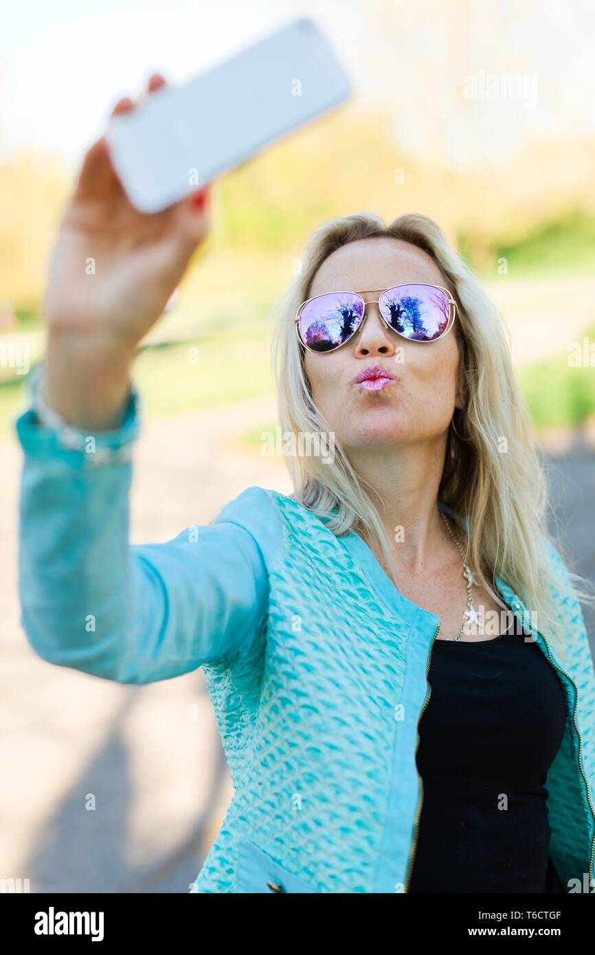 Donna bionda con occhiali da sole rendendo selfie con smart phone Foto  stock - Alamy