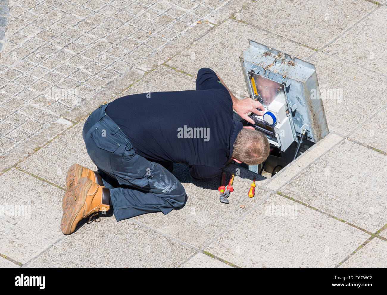Uomo a terra sollevando una pavimentazione schiaffo per eseguire la manutenzione NEL REGNO UNITO. Foto Stock
