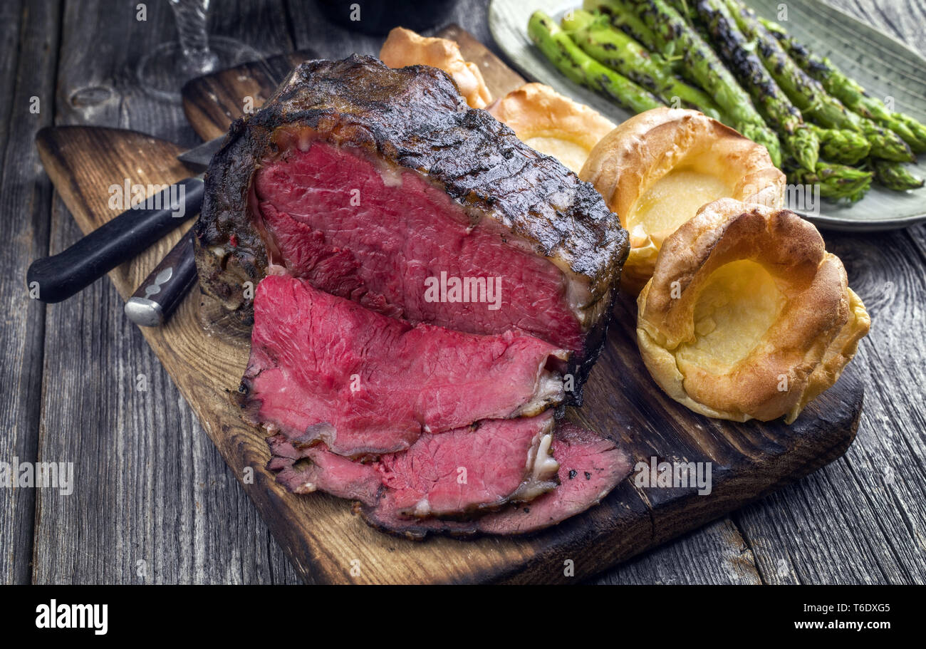 Barbecue secca nervatura invecchiato di manzo con asparagi verdi e Yorkshire pudding come close-up su una vecchia scheda di taglio Foto Stock