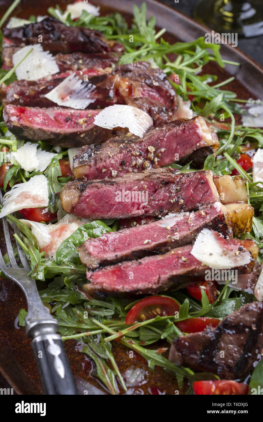 Italiano tradizionale di Tagliata di Manzo con parmigiano e insalata come close-up su una piastra Foto Stock