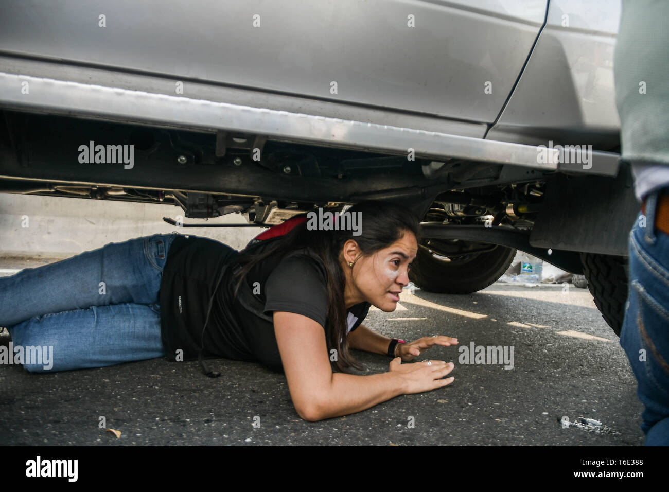 Una donna visto che si nasconde sotto una macchina per evitare i proiettili. Militare venezuelano che sostengono il venezuelano leader dell opposizione Juan Guaido ha preso per la strada con le loro armi insieme con anti governo manifestanti in un colpo di stato militare contro il governo socialista guidato da presidente Nicolas Maduro. Foto Stock