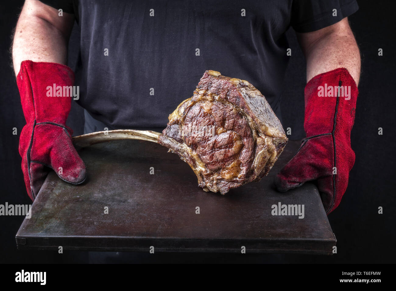 L uomo è in possesso di un Barbecue Wagyu Tomahawk bistecca su vecchio foglio di metallo nelle sue mani con guanti Foto Stock